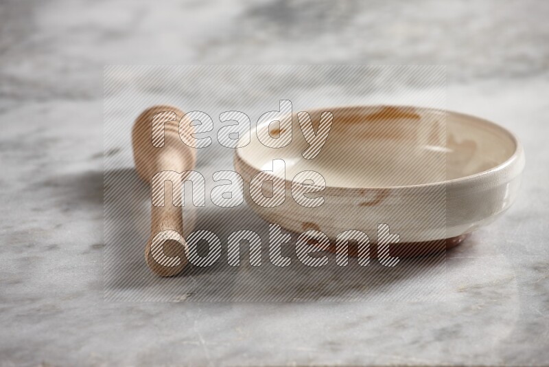 Beige pottery bowl with wooden honey dipper on the side on grey marble background