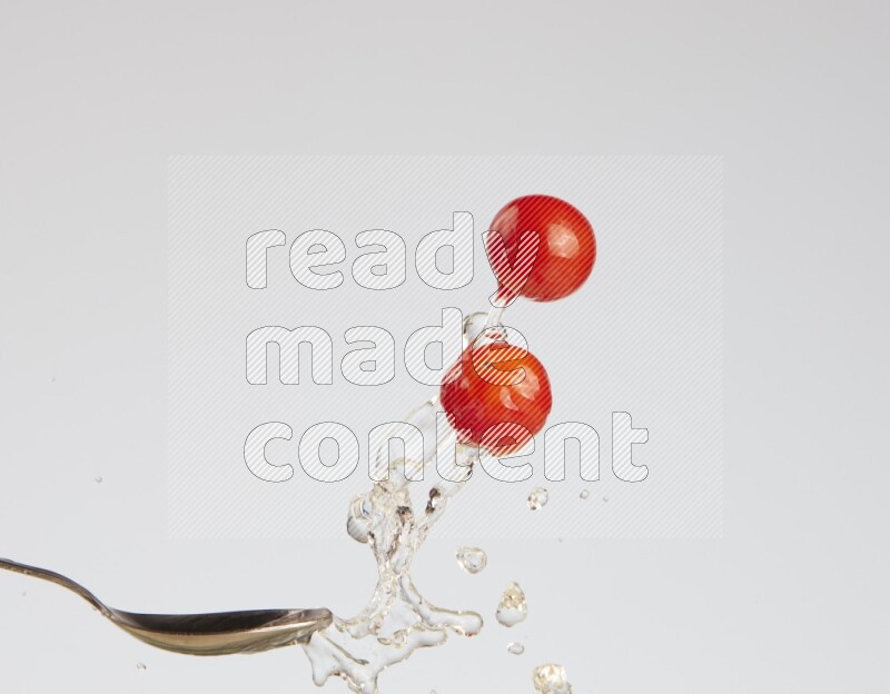 A metal spoon throwing two cherry tomatoes leaving a splash of water behind on a light blue background
