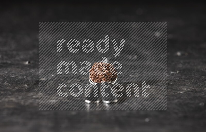 ملعقتان معدنيتان ممتلئتان بحبوب بذر الكتان علي خلفية سوداء