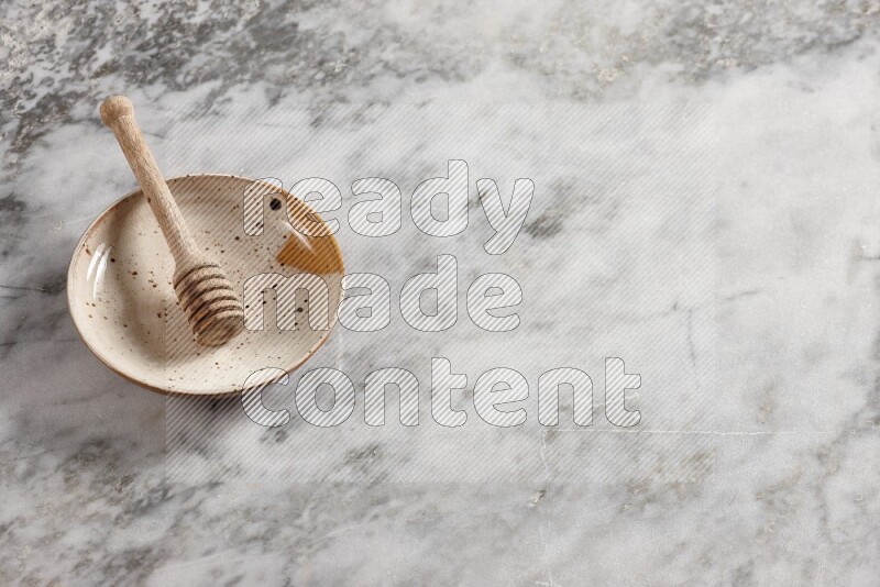 Multicolored pottery plate with wooden honey dipper in it on grey marble background
