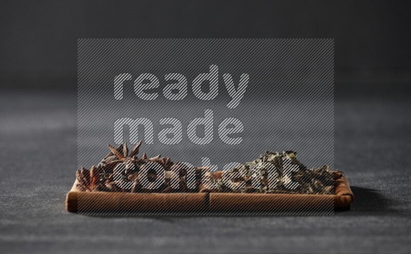 مربعان من أعواد القرفة ممتلئان باليانسون النجمي والريحان المجفف علي خلفية سوداء