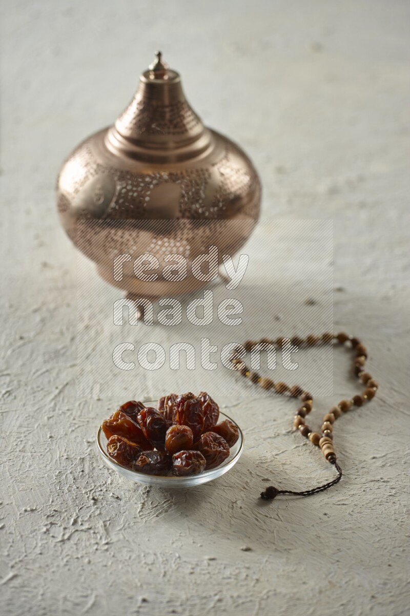 A golden lantern with different drinks, dates, nuts, prayer beads and quran on textured white background