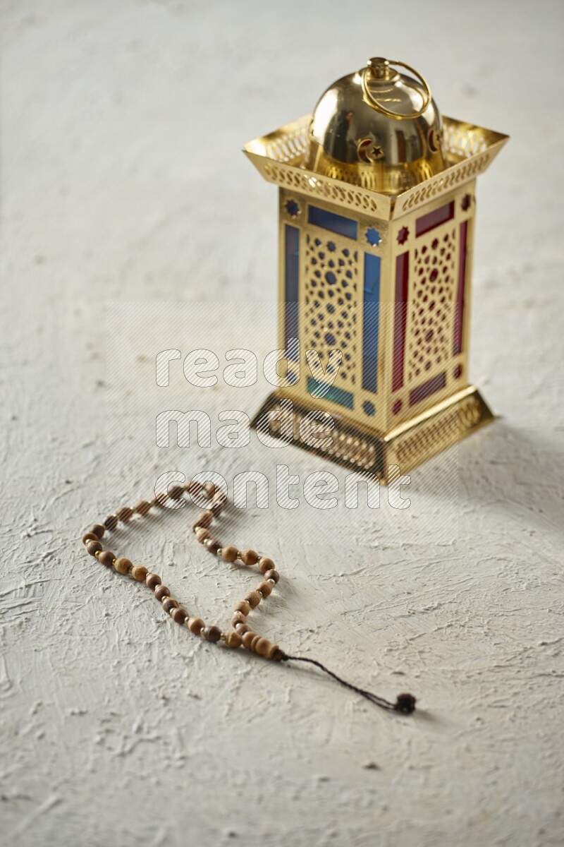A golden lantern with different drinks, dates, nuts, prayer beads and quran on textured white background