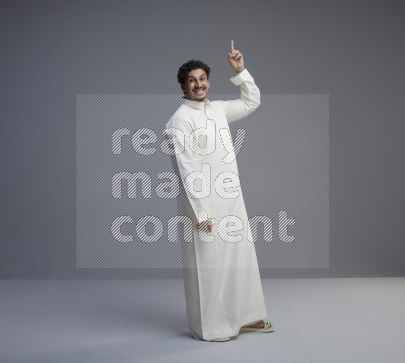 A Saudi man standing wearing thob interacting with the camera on gray background