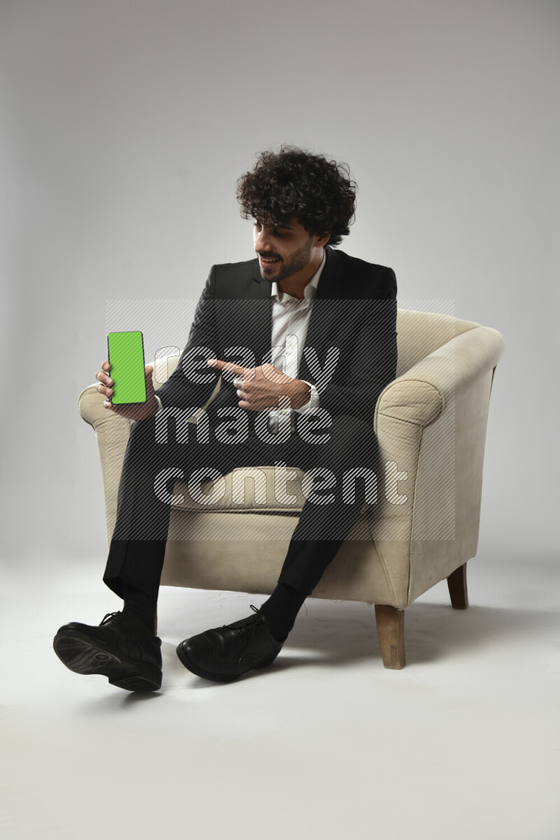 A man wearing formal sitting on a chair showing a phone screen on white background