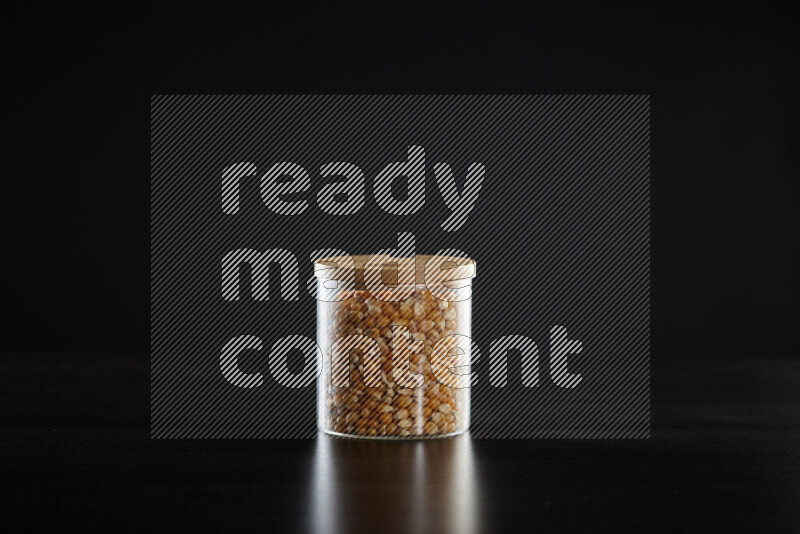 Dry corn kernels in a glass jar on black background