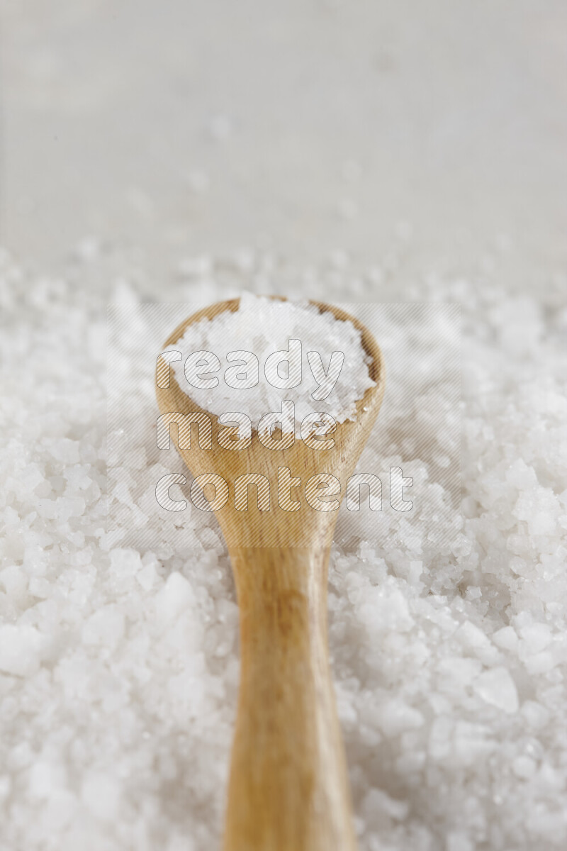 A wooden spoon full of white salt on white background