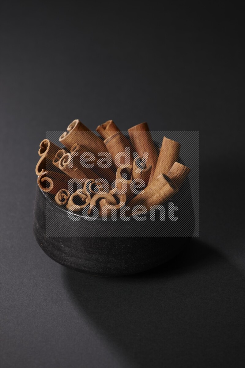 Cinnamon sticks in a black bowl on a black background in different angles