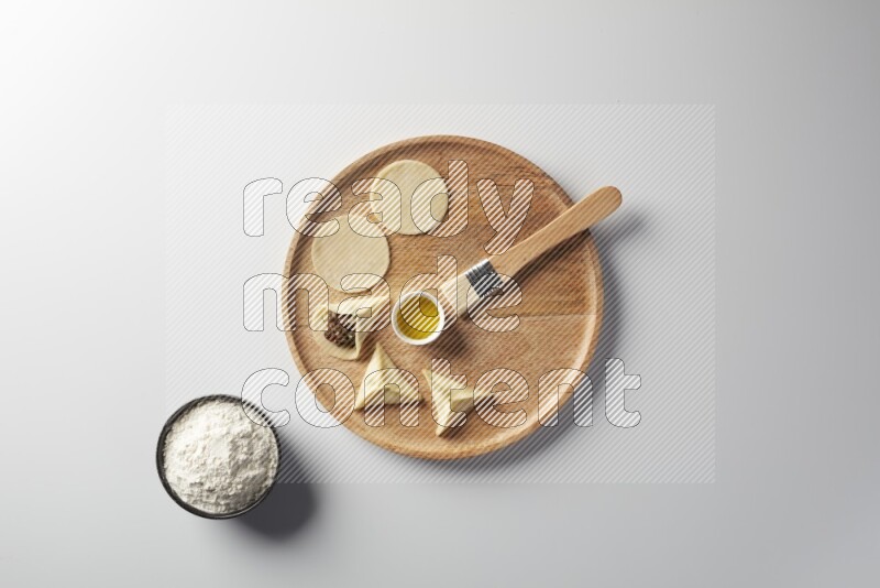 two closed sambosas and one open sambosa filled with meat while flour, and oil with oil brush aside in a wooden dish on a white background