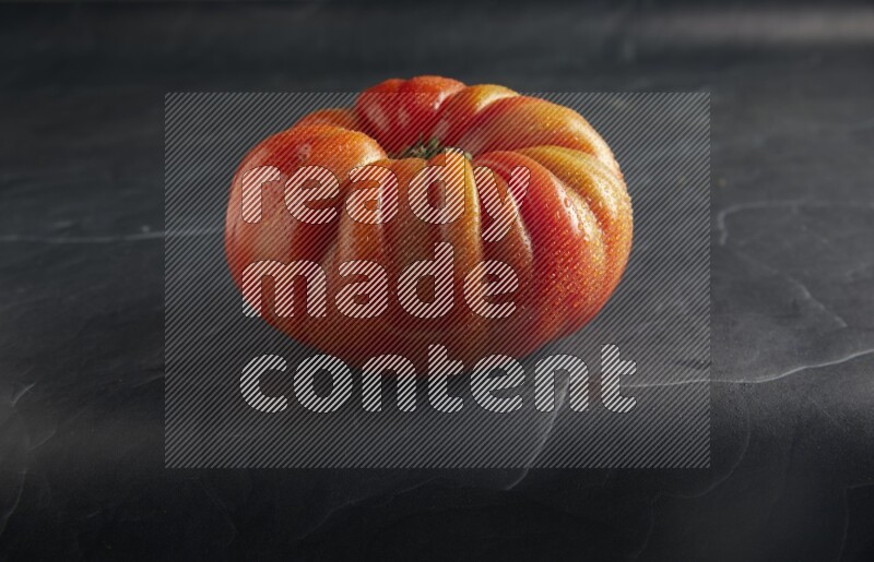45 degree single heirloom tomato on a textured black slate background