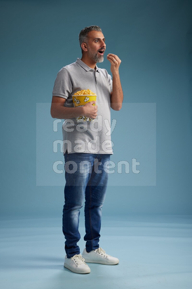 Man Standing eating popcorn on blue background