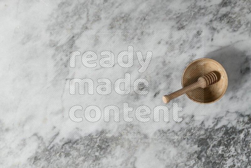 Beige pottery bowl with wooden honey dipper in it on grey marble background