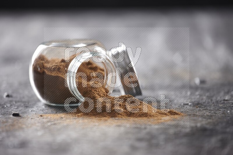 Flipped herbal glass jar full of cinnamon powder on textured black background