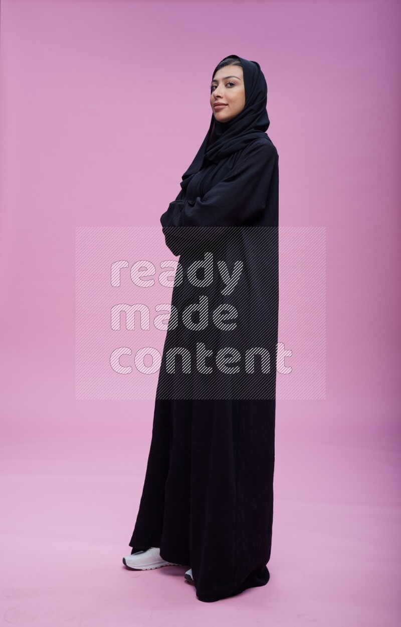 Saudi woman wearing Abaya standing with crossed arms on pink background