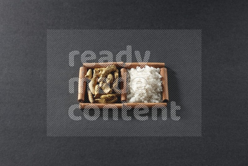 مربعان من أعواد القرفة ممتلئان بالملح الأبيض وأصابع الكركم علي خلفية سوداء