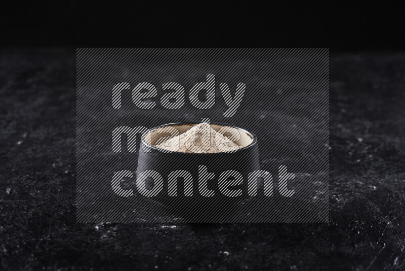 A black pottery bowl full of onion powder on black background