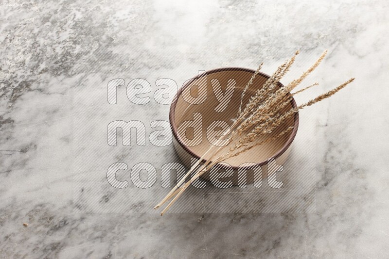 Wheat stalks on beige pottery oven bowl on grey marble background