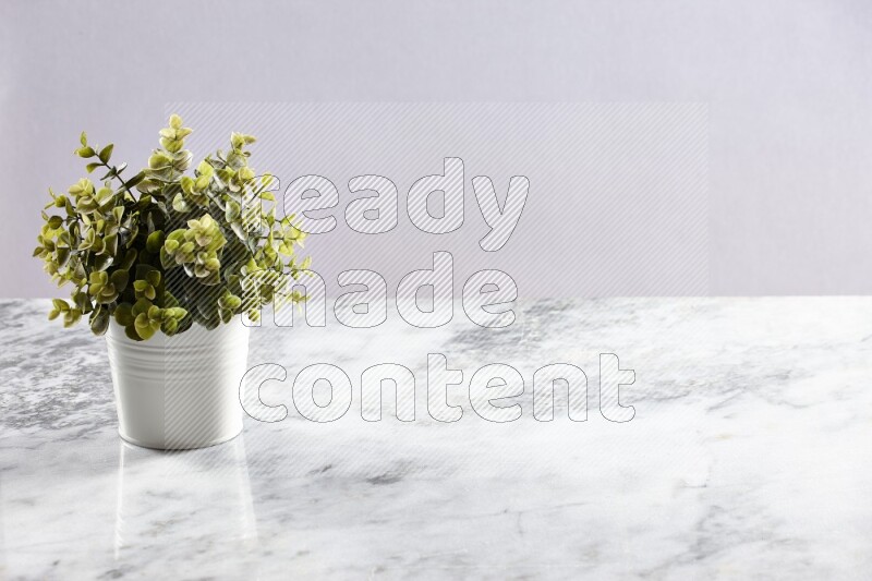 Green artificial plant in white pot on light grey marble background