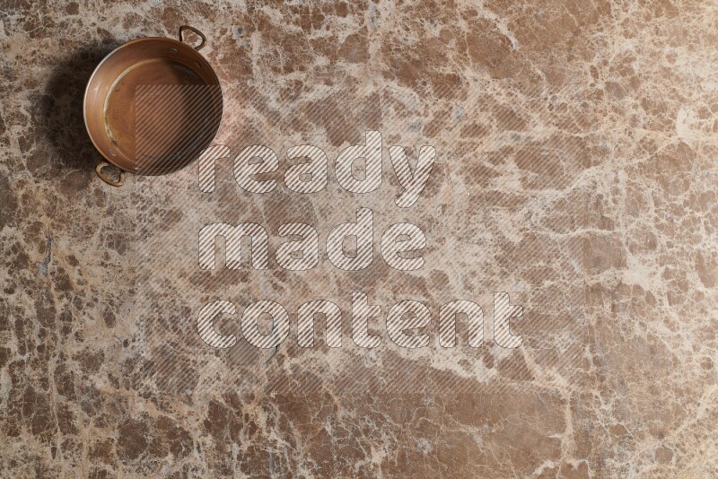 A small copper pan on beige marble background
