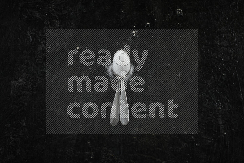 2 metal spoons filled with white salt on black background