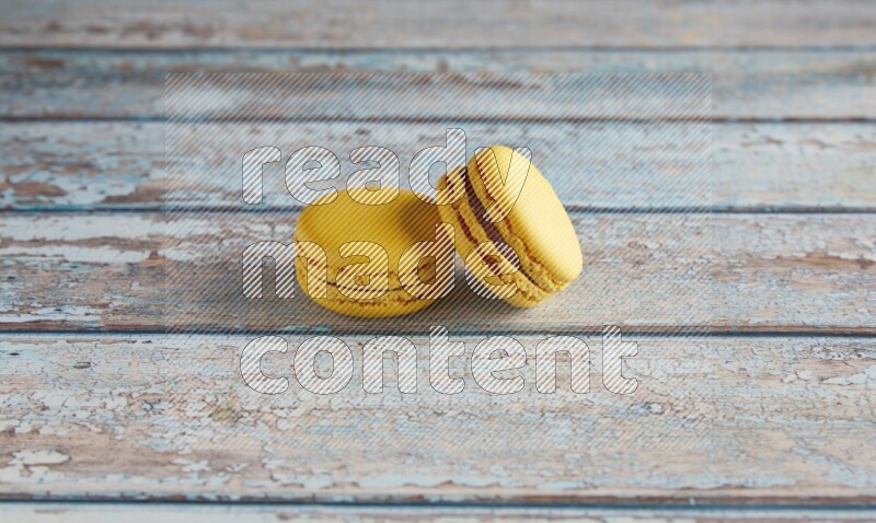45º Shot of two Yellow Lemon macarons on light blue wooden background