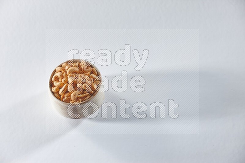 A beige ceramic bowl full of cashews on a white background in different angles