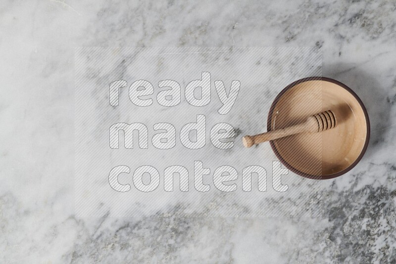 Beige pottery oven plate with wooden honey dipper in it on grey marble background