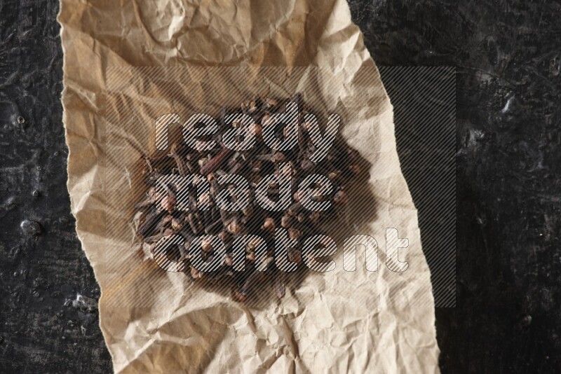 Cloves in crumpled piece of paper on a textured black flooring