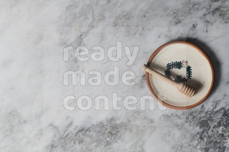 طبق فخاري مزخرف مع ملعقة عسل خشبية بداخله على خلفية من الرخام الرمادي