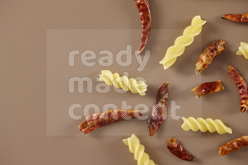 Raw pasta with different ingredients such as cherry tomatoes, garlic, onions, red chilis, black pepper, white pepper, bay laurel leaves, rosemary and cardamom on beige background