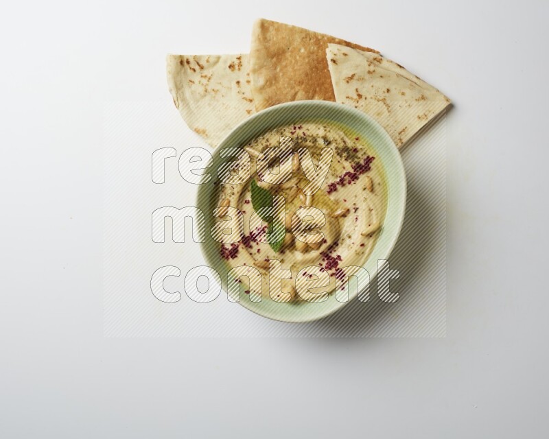 Hummus in a green plate garnished with zattar & sumak on a white background