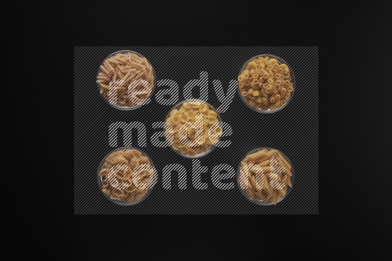 Different pasta types in 5 glass bowls on black background