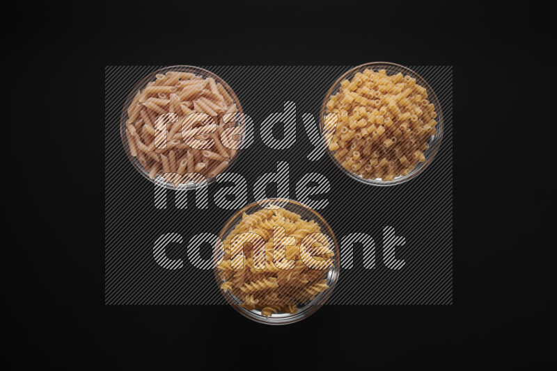 Different pasta types in glass bowls on black background