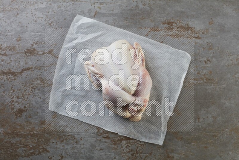 whole raw chicken on a parchment paper direct on a rustic grey background
