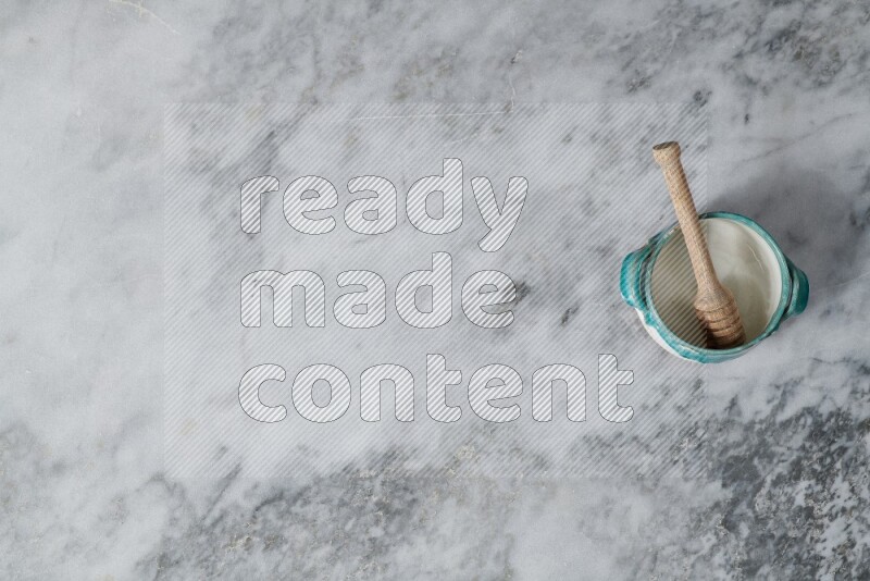 وعاء فخاري متعدد الألوان مع ملعقة عسل خشبية بداخله على خلفية من الرخام الرمادي