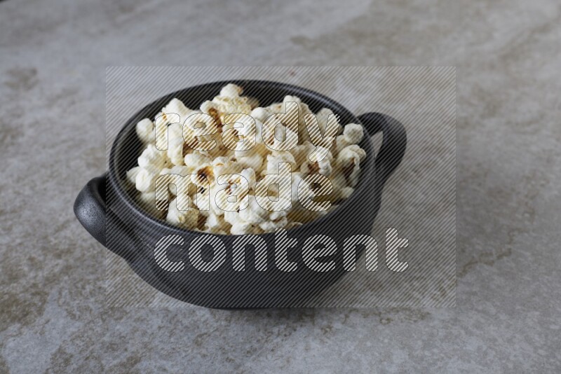 popcorn in a black handheld ceramic bowl on a grey textured countertop