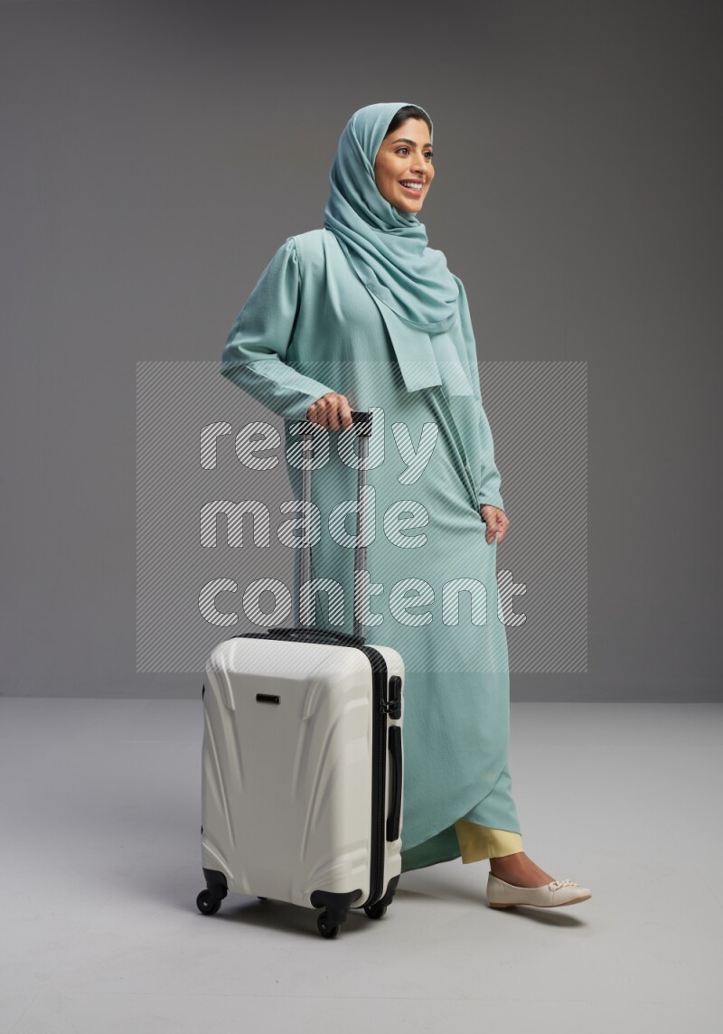 Saudi Woman wearing Abaya standing holding Travel bag on Gray background