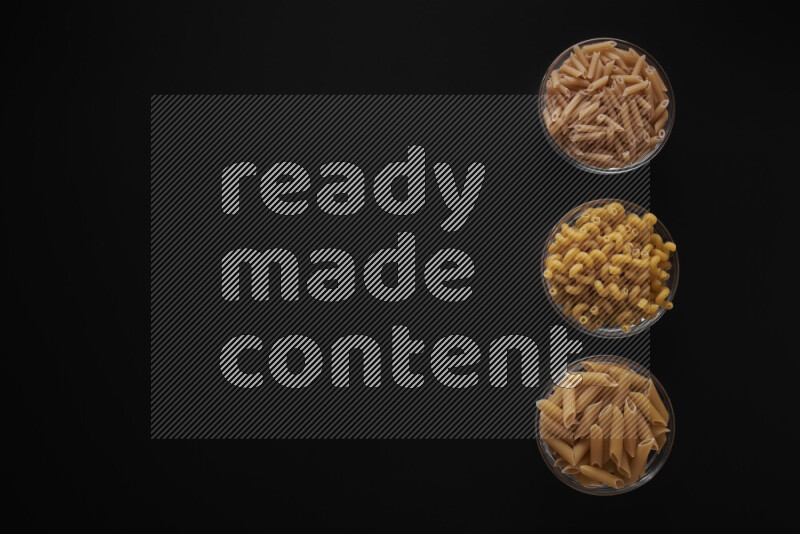 Different pasta types in 3 glass bowls on black background