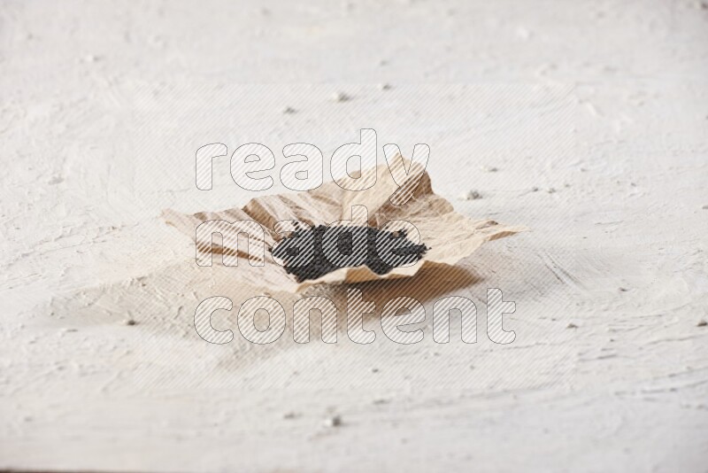 A crumpled piece of paper full of black seeds on a textured white flooring