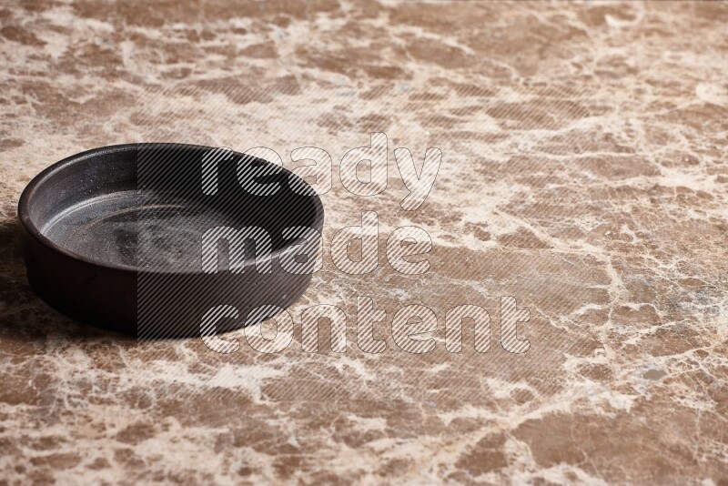 A black pottery oven plate on beige marble background