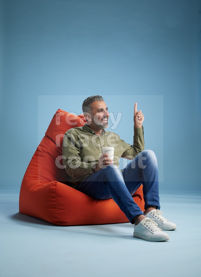 A man sitting on an orange beanbag and drinking coffee
