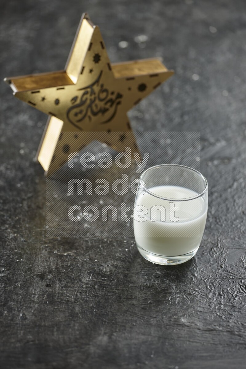 A wooden golden star lantern with different drinks, dates, nuts, prayer beads and quran on textured black background