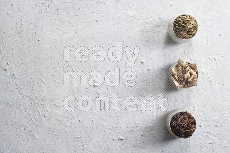 Cardamom, ginger and star anise in 3 bowls on a textured white background