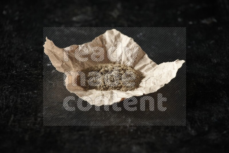 Cardamom powder in a crumpled piece of paper on textured black flooring