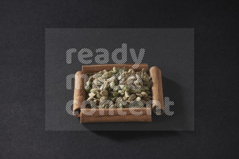 A single square of cinnamon sticks full of Cardamom on black flooring
