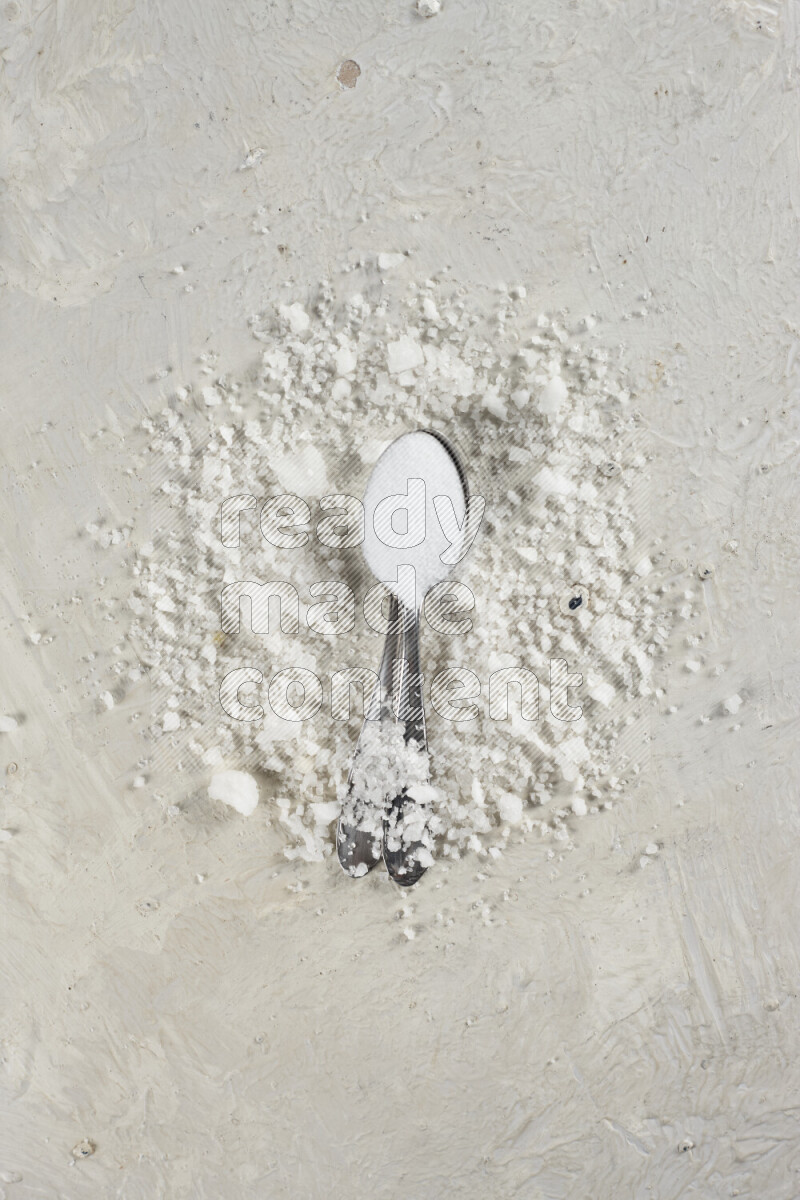 ملعقتان معدنيتان ممتلئتان بملح الطعام الناعم وملح الهايمالايا الناعم على خلفية بيضاء