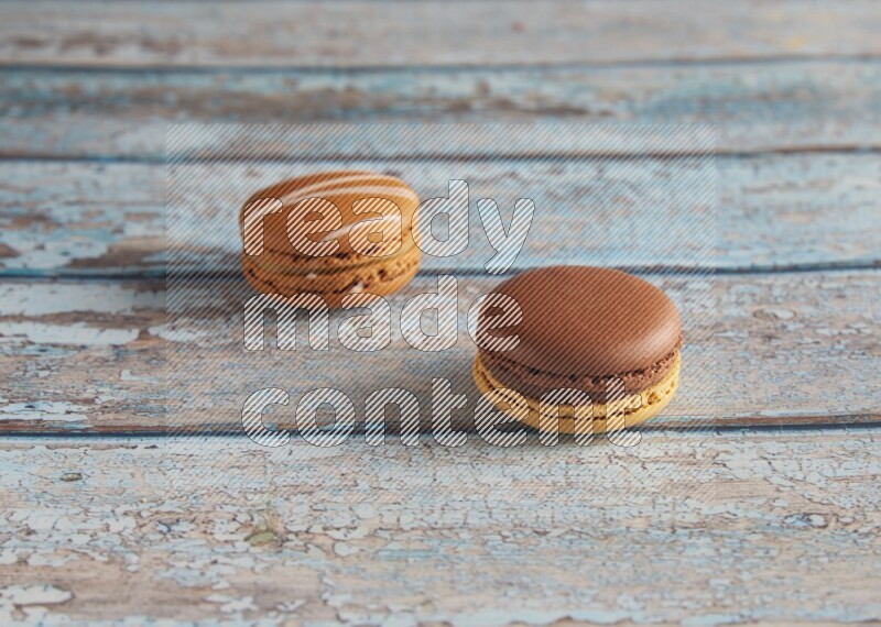 45º Shot of of two assorted Brown Irish Cream, and Yellow, and Brown Chai Latte macarons  on light blue background