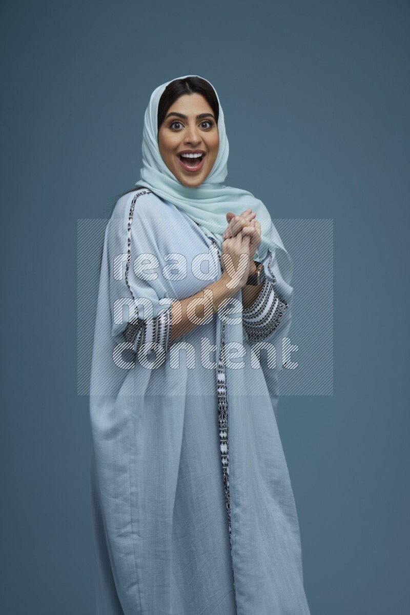 A woman posing in a blue background wearing a blue Abaya with hijab