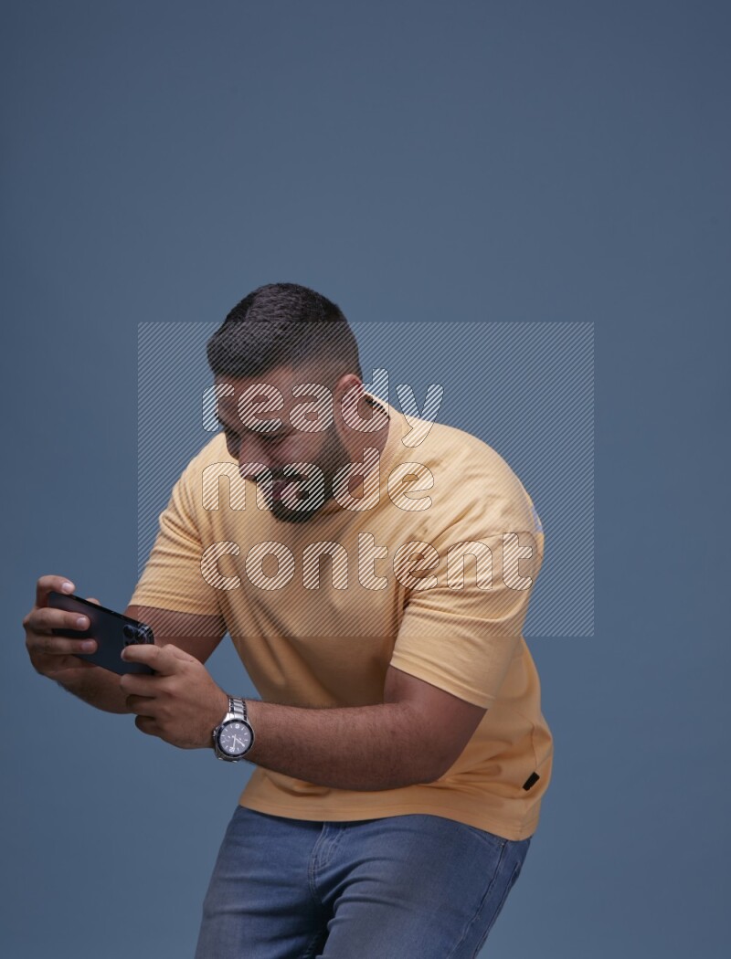 A man Playing Games on Smartphone on Blue Background wearing Orange T-shirt