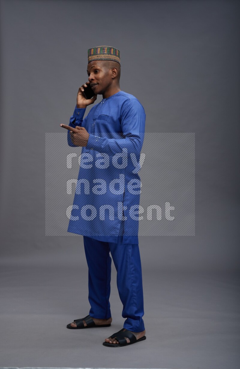 Man wearing Nigerian outfit standing talking on phone on gray background